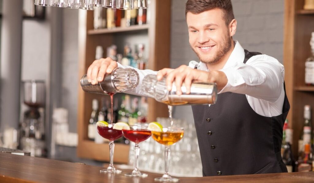 Attractive young barman is making drinks in pub