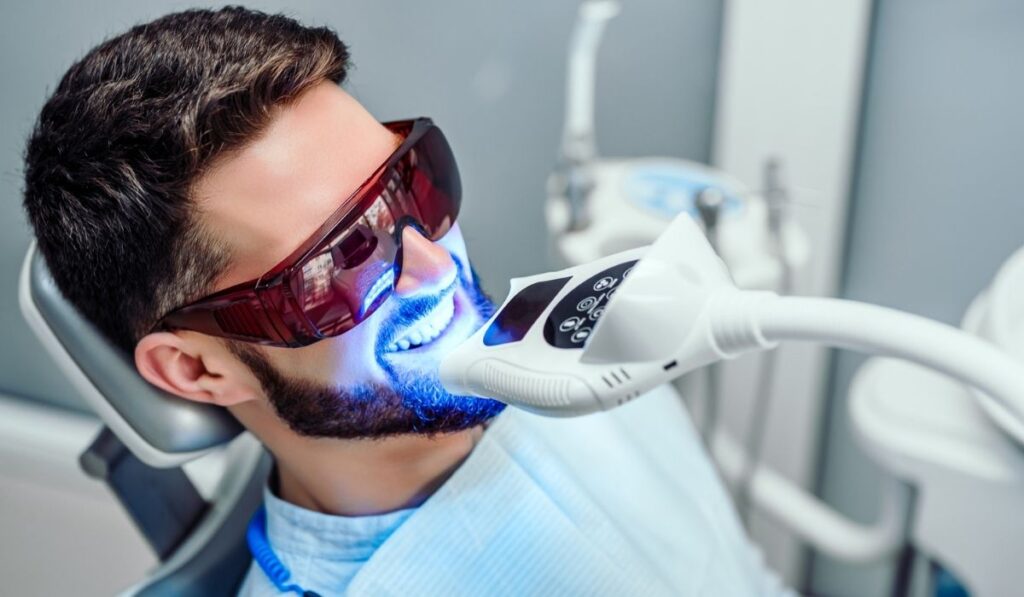 Dentist starting teeth whitening procedure with young man 