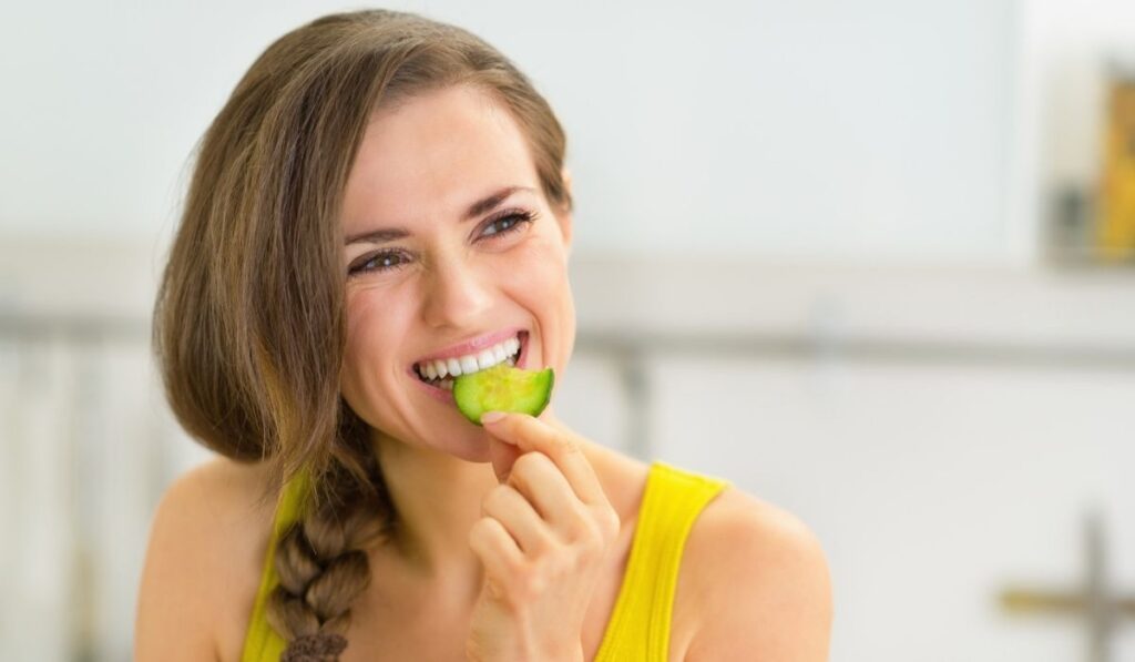 Portrait of woman eating cucumber in kitchen