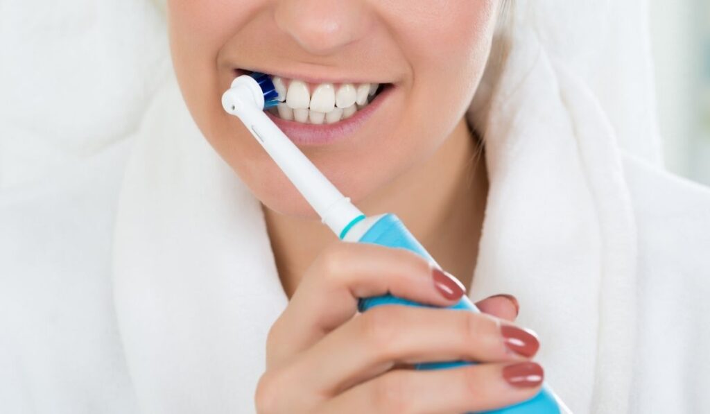 Woman In Bathrobe Brushing Teeth With Electric Toothbrush