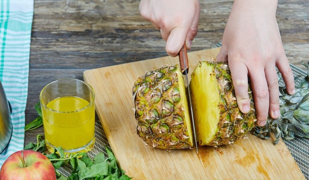 Woman cutting a fresh pineapple on a wooden cutting board 