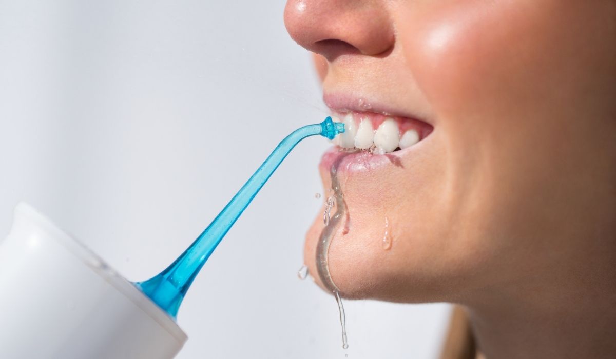 Woman with perfect white smile using portable water flosser or oral irrigator