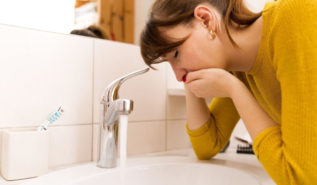 Young vomiting woman near sink in bathroom