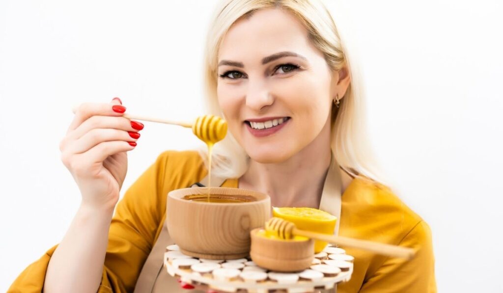 Smiling young woman with bowl of honey on white background
