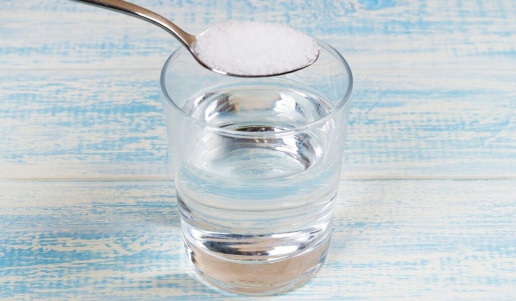 Glass of water with tea spoon full of salt above 