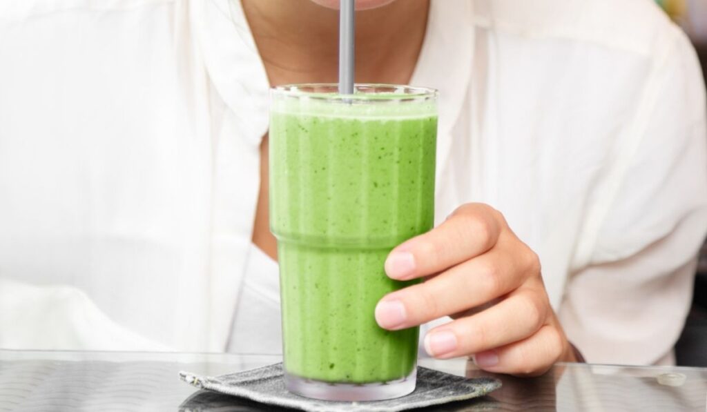 Matcha green tea smoothie cold dessert shake drink woman drinking with straw at cafe table