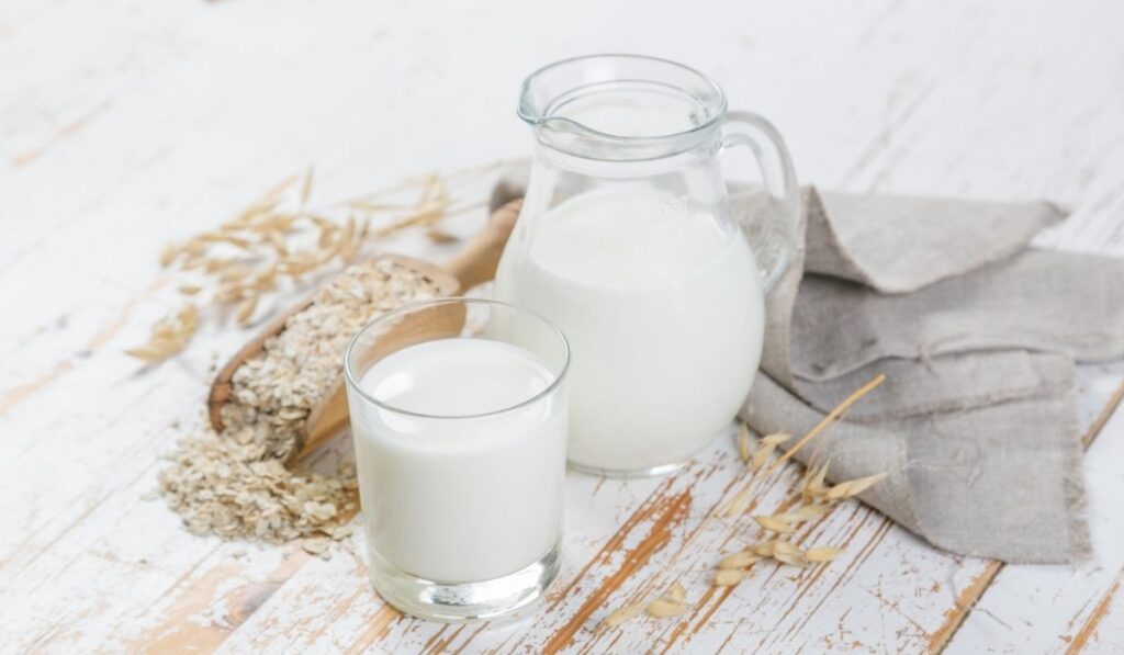Oat milk in glass and jar on wood background 