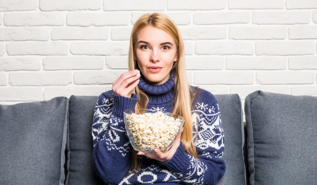 Portrait of beautiful young woman eating popcorn while watching movie in living room