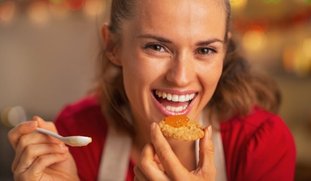 Portrait of smiling young housewife eating orange jam 