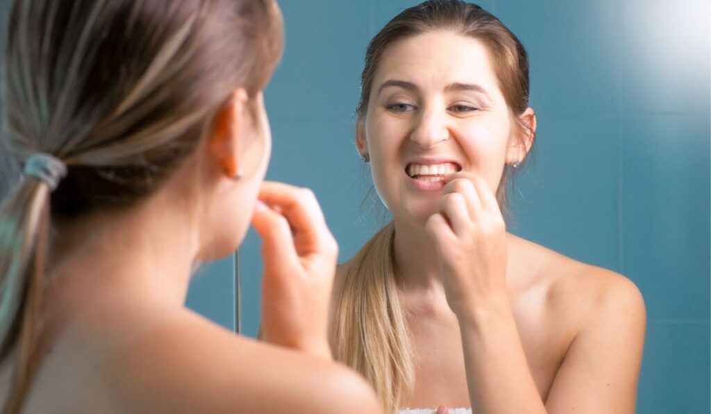 Portrait of young woman checking her teeth at mirror 