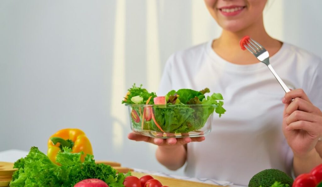 Woman hands holding salad bowl with eating tomato and various green leafy vegetables on the table at the home
