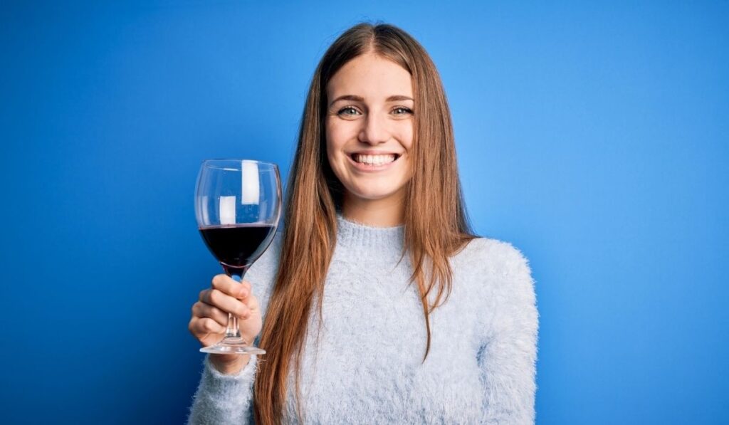 Young beautiful redhead woman drinking glass of red wine 