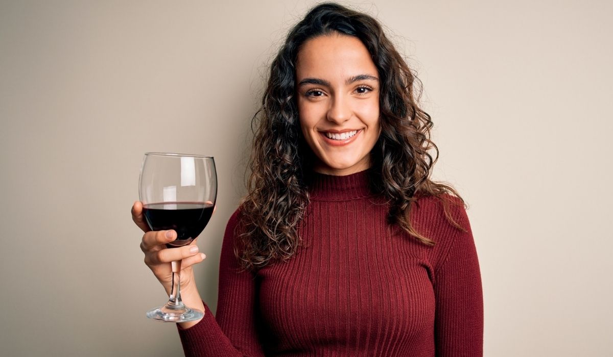 Young beautiful woman with curly hair drinking glass of red wine