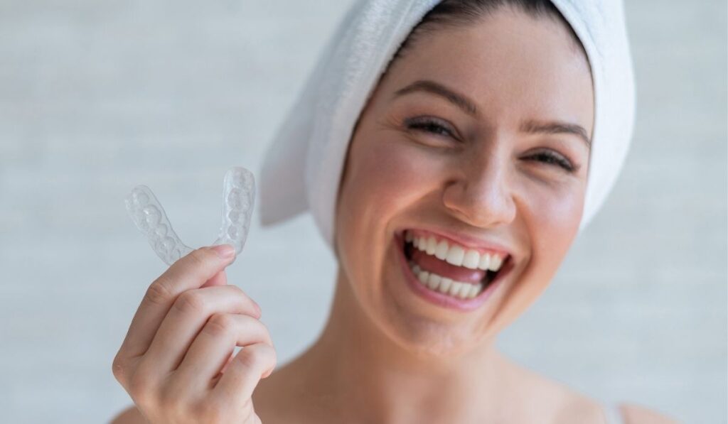A woman with a towel on her head holds a whitening mouth guard for teeth 