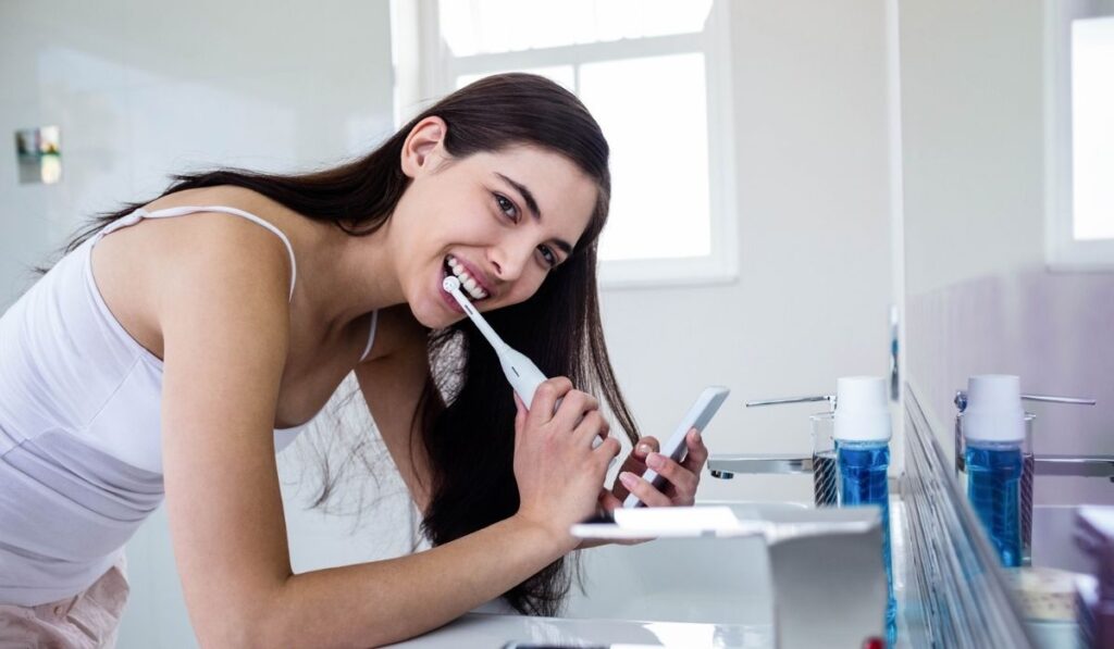 Brunette using smartphone while brushing teeth