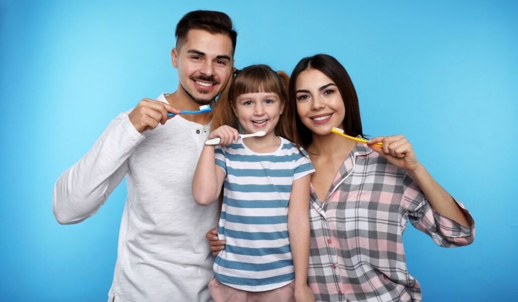 Little girl and her parents brushing teeth together 