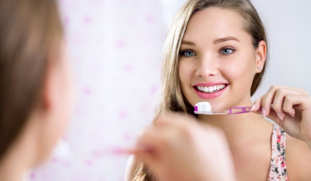Pretty female looking in mirror while brushing teeth 