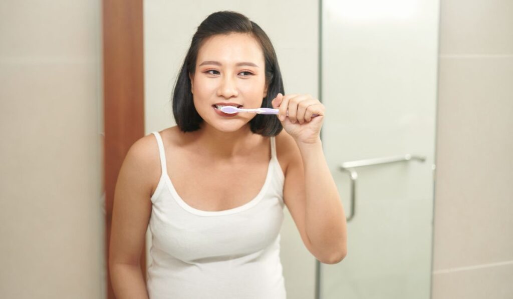 Beautiful young woman brushing her teeth in morning 