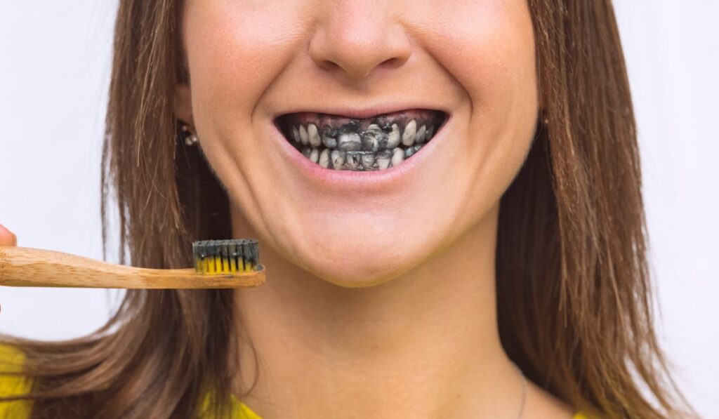 Close up of smiling woman brushing teeth with eco friendly bamboo toothbrush with black charcoal whitening toothpaste 