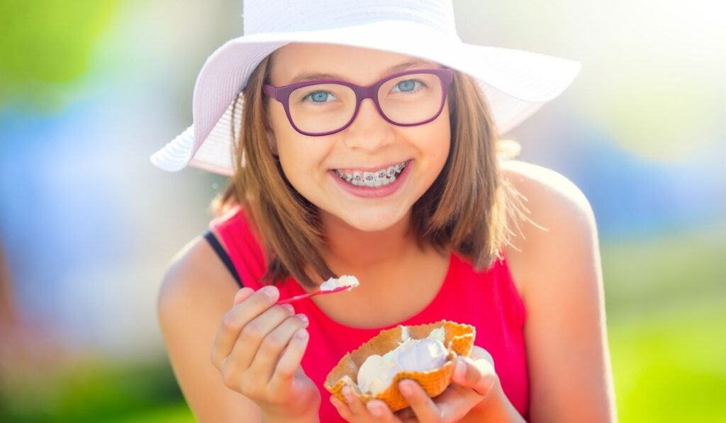 Cheerful teenage girl with dental braces glasses and ice cream 