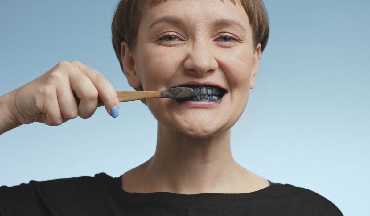 Pretty young woman brushing her teeth with black toothpaste