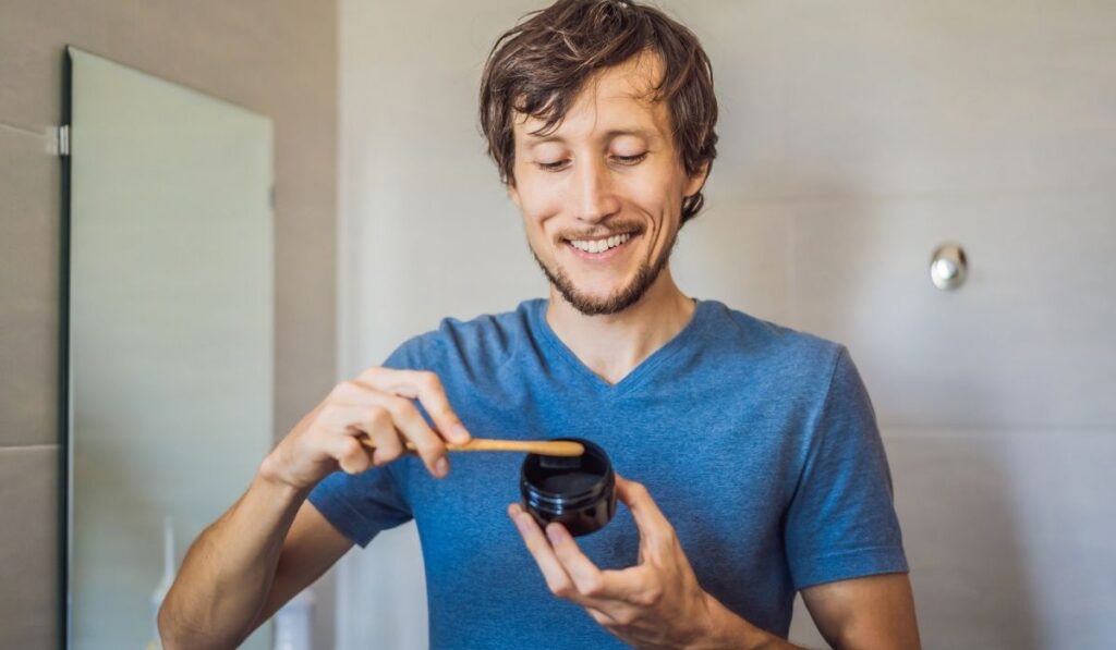 Young man brush teeth using Activated charcoal powder for brushing and whitening teeth