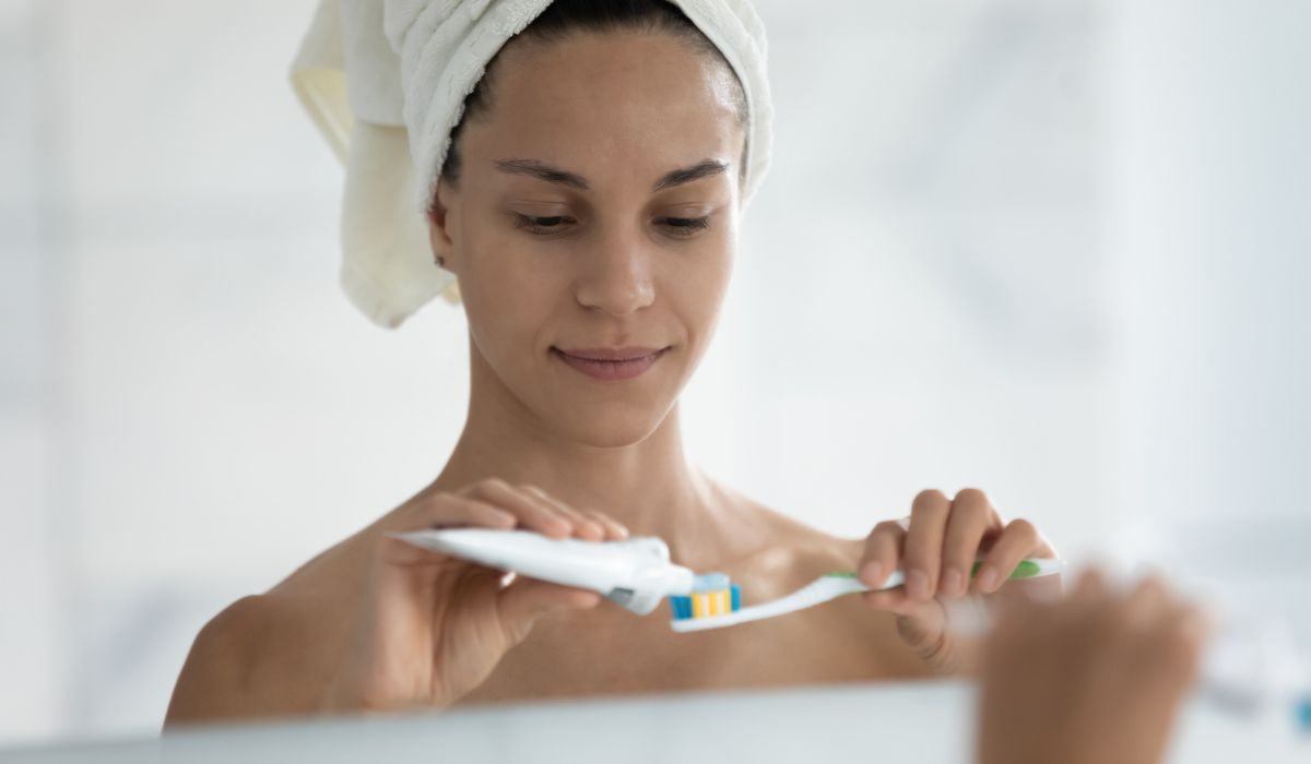 Head shot mirror reflection beautiful woman applying toothpaste on toothbrush