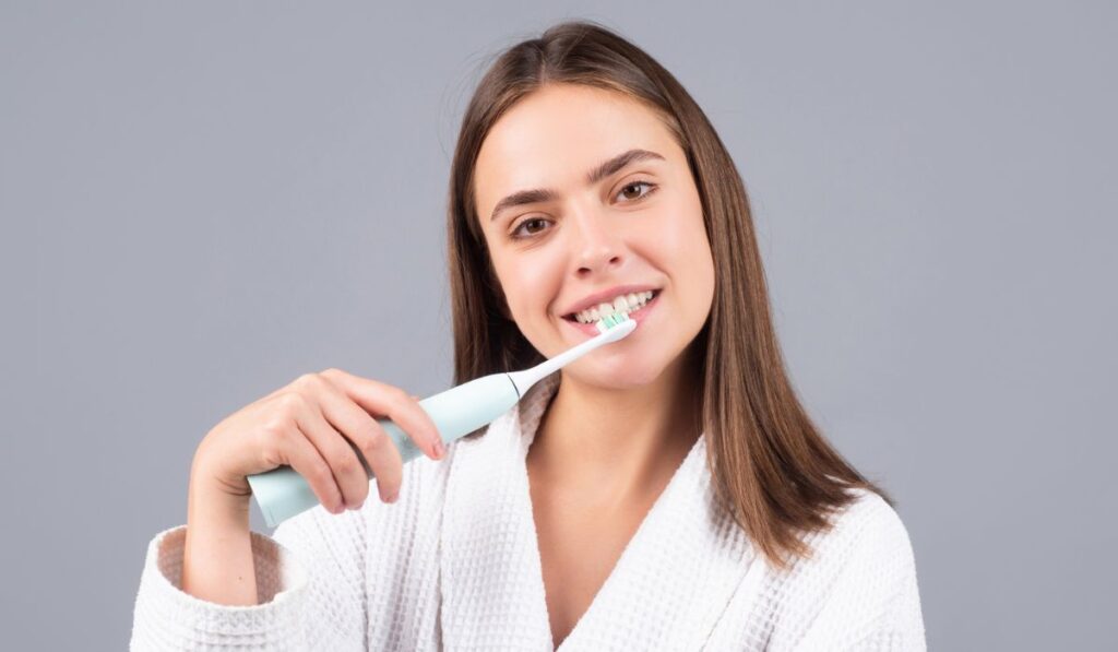 Smiling young woman brushing teeth using toothbrush with whitening toothpaste