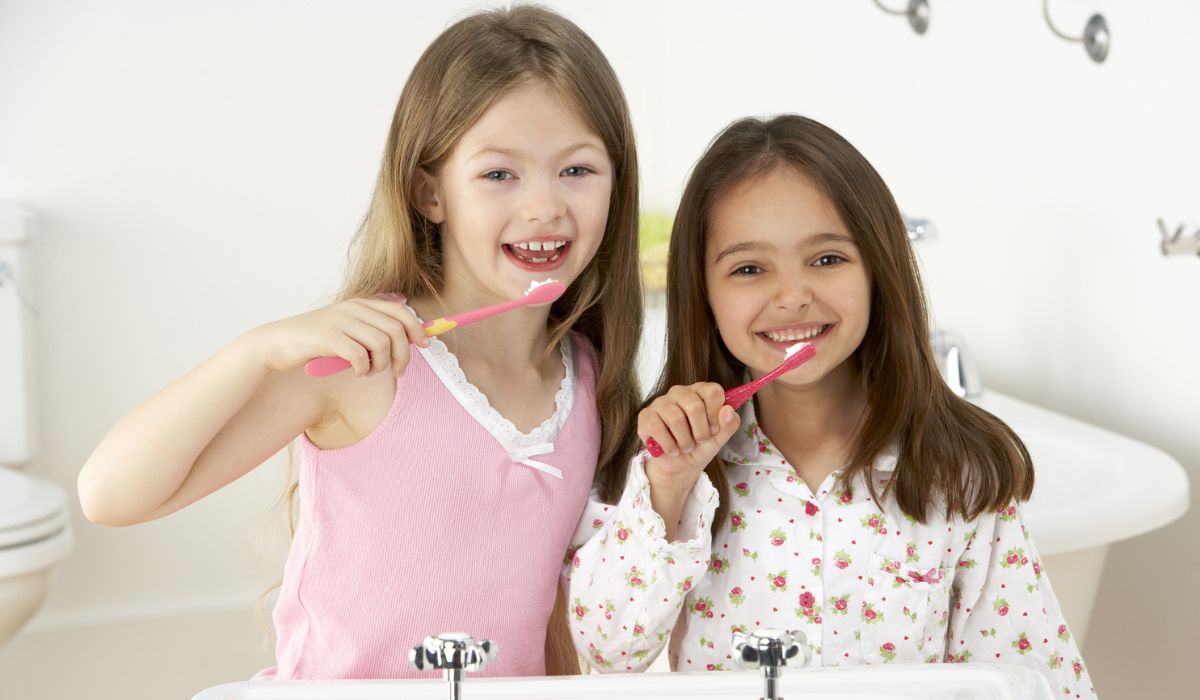 Two Young Girls Brushing Teeth at Sink Looking Pretty And Happy