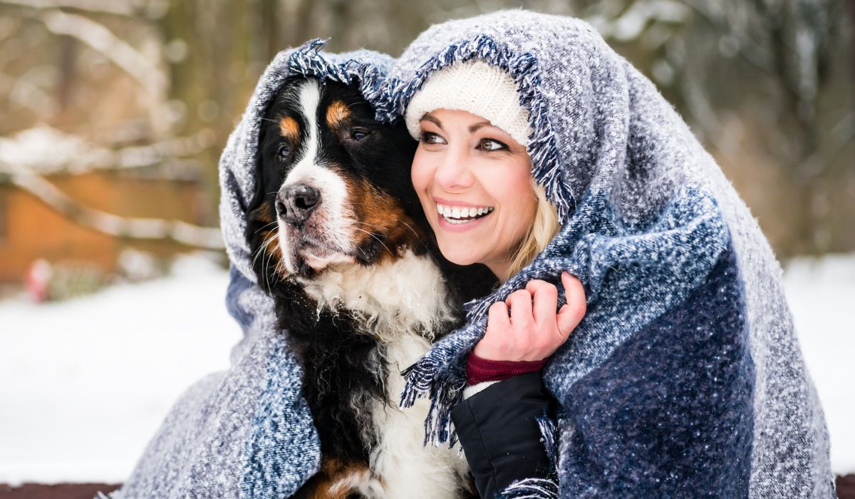 Woman and her dog getting warm on cold winter day under a blanket snuggling