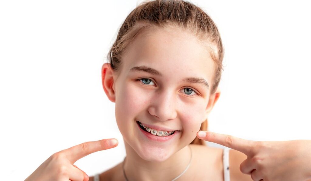 Teenage girl smiling in orthodontic brackets showing OK sign