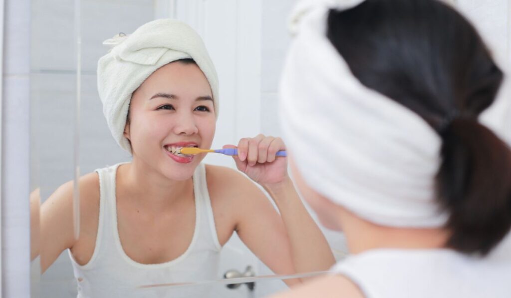Young asian woman brushing her teeth at the mirror