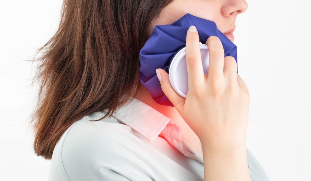 A girl attaches a medical bag with cold to the swelling on her cheek after removing a wisdom tooth