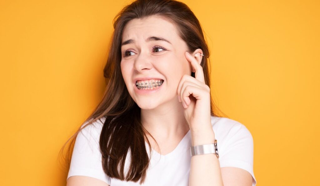 Attractive girl with braces grimaces from pain in her teeth