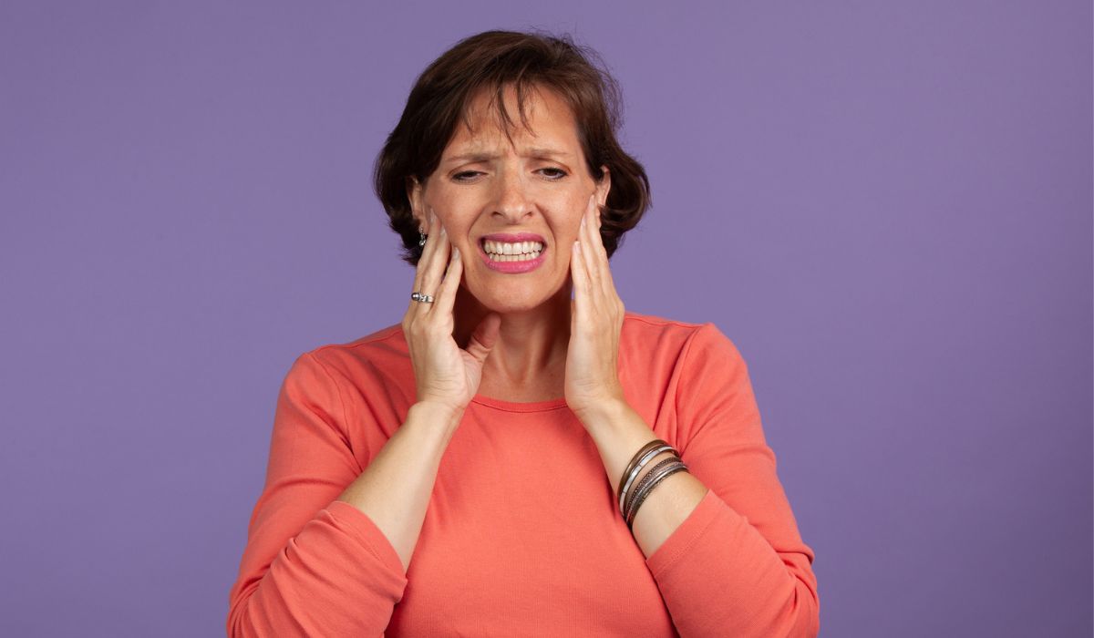 Middle Aged woman with TMJ pain holding her jaw and making a pained expression