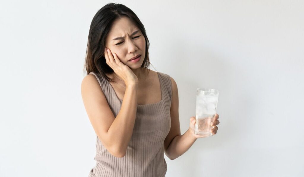 Young Asian woman suffering from toothache and hand holding glass of cold water with ice