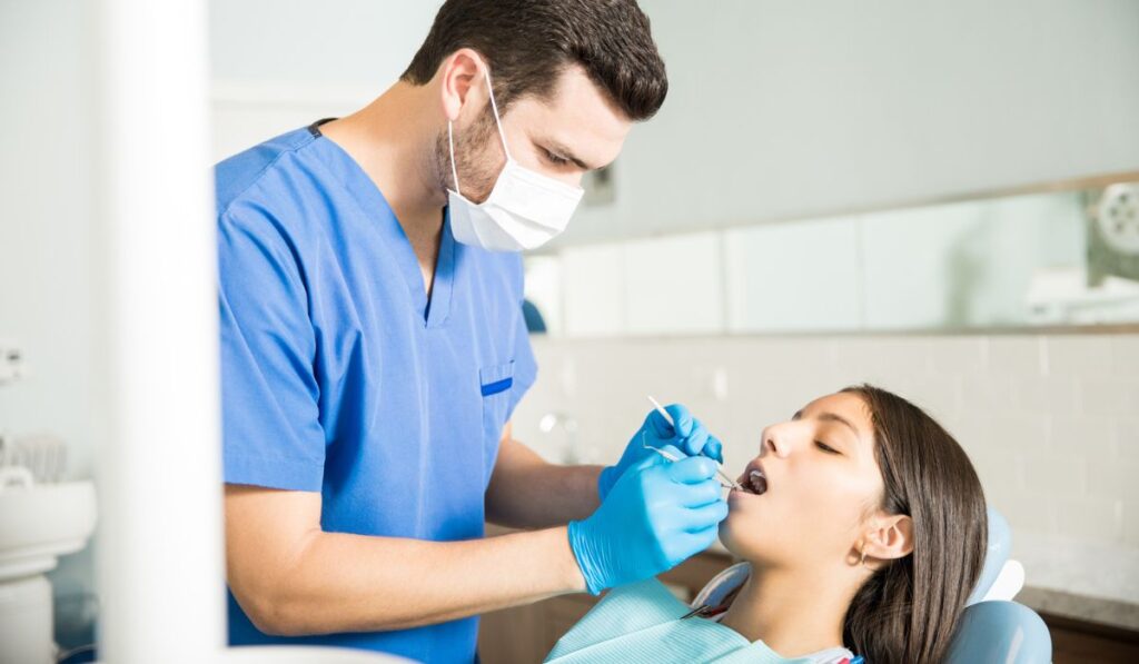 Dentist Examining Teenage Girl With Dental Tools At Clinic