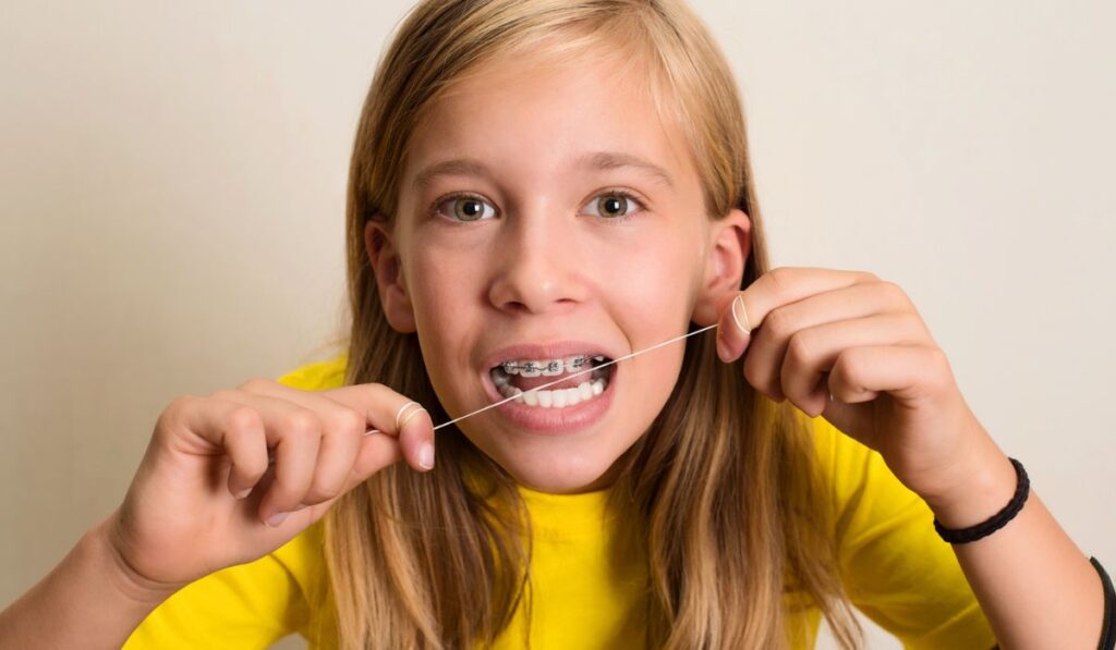 Funny girl with dental braces flossing her teeth